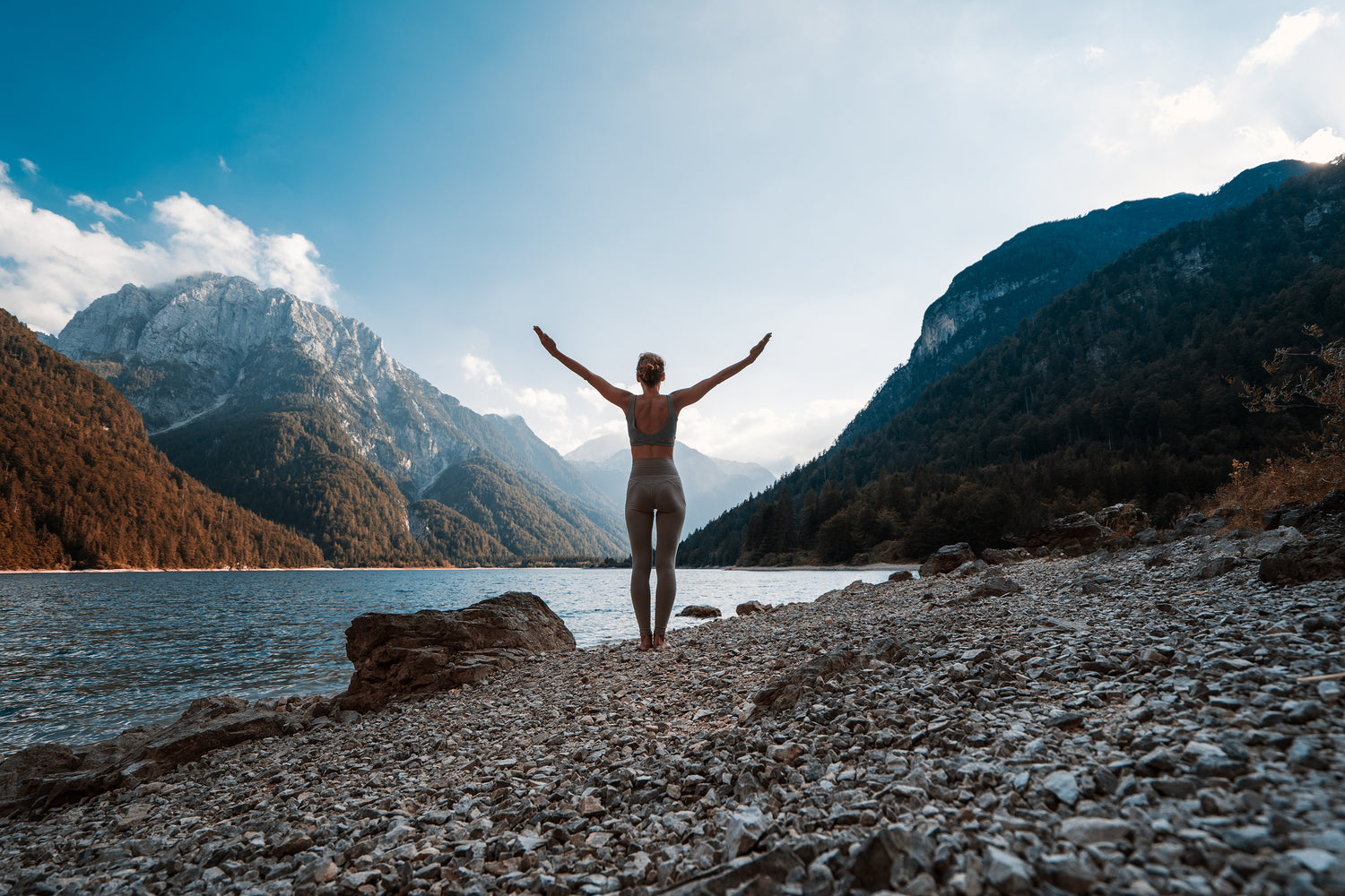 fit young woman in activewear set doing a yoga pose facing a beautiful mountain scenery