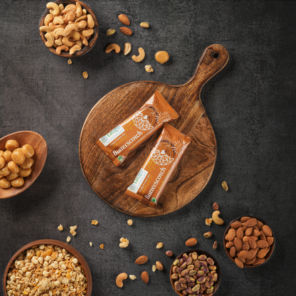 Linafsi - crispy protein bar - butterscotch - lifestyle image of bar on wooden tray surrounded by pistachios, cashews, almonds, butterscotch candies and oats