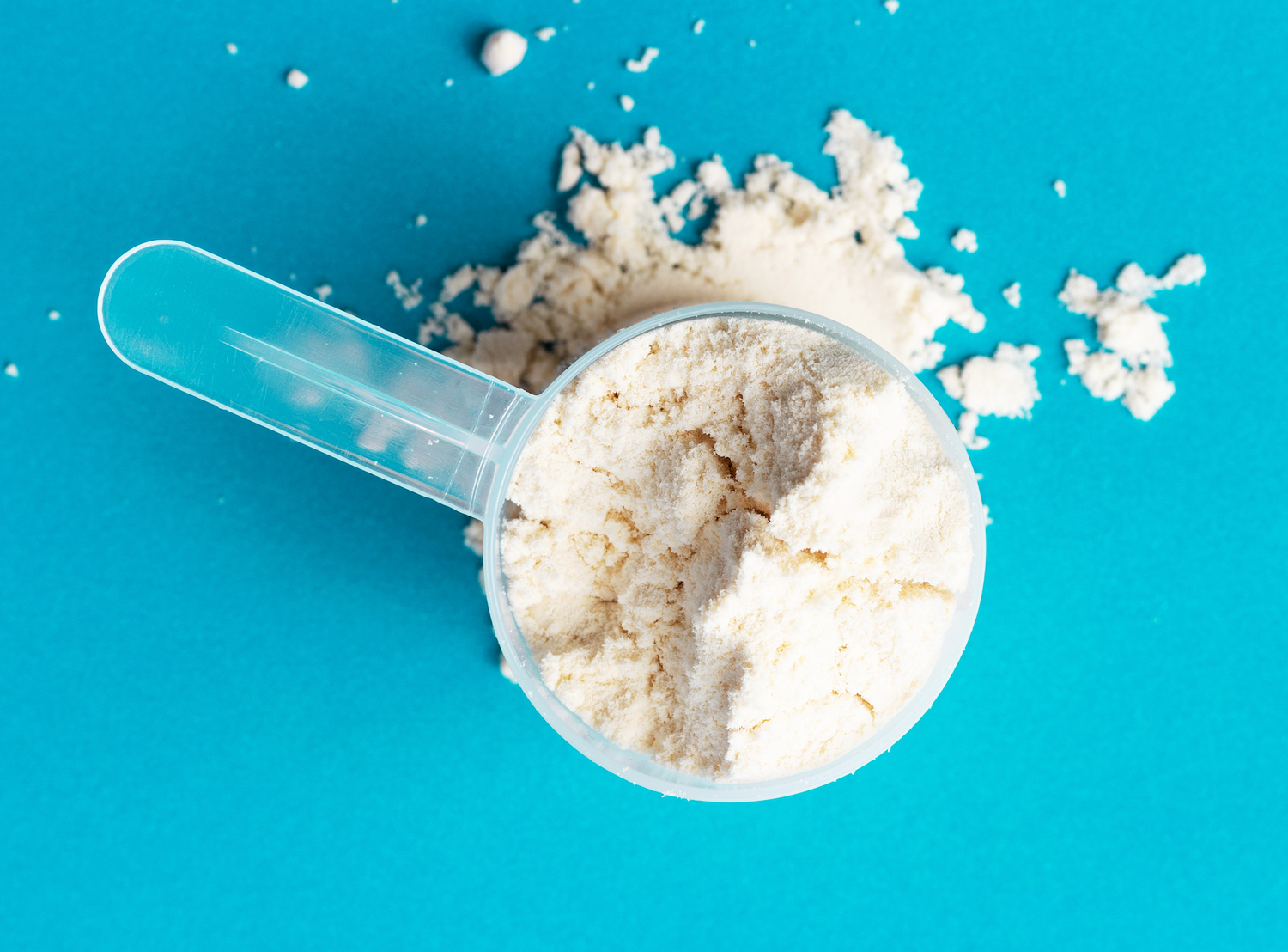 Scoop of vanilla whey protein powder on bright background